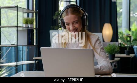 Fröhlich motiviertes weißes Mädchen Geschäftsfrau hört Musik in Kopfhörern Arbeiten mit Laptop moderner Tech Service Geschäftsfrau sitzen am Tisch weiblich Stockfoto