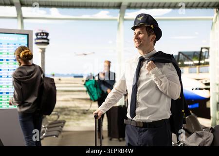 Flugkapitän in Uniform, der mit Koffern durch das geschäftige Flughafenterminal geht und sich auf den Flug vorbereitet. Professioneller Pilot verkörpert die Karriere in der Luftfahrt und verlässlichen Service im Flugbegleiterbetrieb. Stockfoto