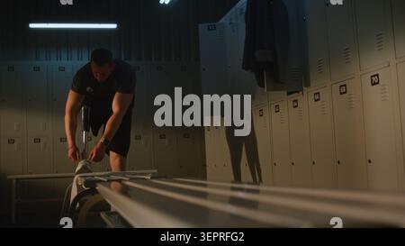 Der entschlossene junge Mann mit Prothetik bereitet sich auf das Training vor, indem er Schnürsenkel auf den weißen Sneaker im Sports Club Dressing Room bindet. Konzept der Resilienz, Vielfalt, reale Menschen, tägliche Routine. Tragbar. Stockfoto