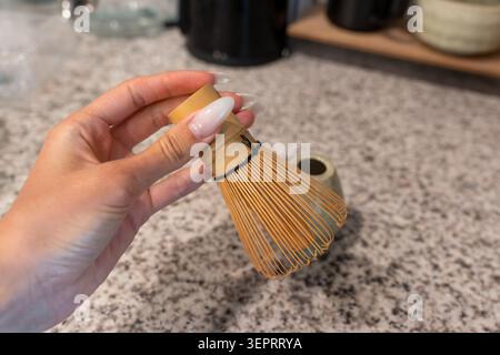 Nahaufnahme einer weiblichen Hand mit Maniküre, die einen Bambus-Matcha-Schneebesen hält und traditionellen Matcha-Tee zubereitet. Japanisches Teezeremonie Konzept, Wellness Stockfoto