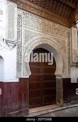 Ein kunstvoller Bogen in der Diwan-Moschee zeigt komplizierten geschnitzten Gips, geometrische Details, dunkle Holzarbeiten und traditionelle marokkanische Handwerkskunst in Fès. Stockfoto