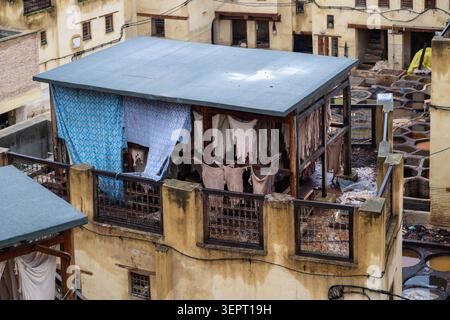 Trocknende Häute hängen von einer Dachwerkstatt über den Gerbbehältern und verwitterten Gebäuden der Sidi Moussa Tannery in Fès, Marokko. Stockfoto