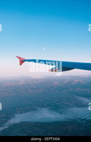 Vertikale Luftaufnahme vom Flugzeugfenster Sitz des Flügels über Neuseelands Berglandschaft und raues Gelände unter blauem Dämmerhimmel mit Mond. Stockfoto