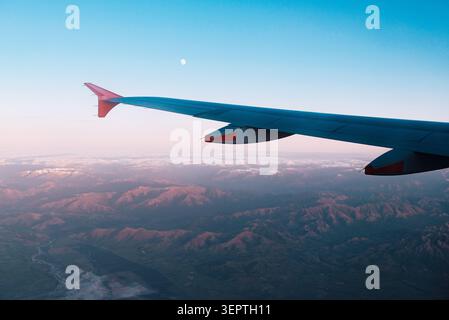 Neuseelands Reise aus der Vogelperspektive des Flügelsitzes über zerklüftete Bergketten und verschneite Täler unter dem rosa Abendhimmel mit Mond. Stockfoto