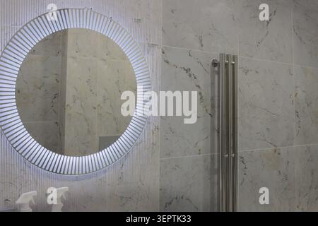 Modernes Bad mit sauberem, elegantem Design. Verchromter Wasserhahn und hoher Kühler sorgen für einen schlanken Kontrast. Das weiße Waschbecken fasst zwei weiße Flaschen Stockfoto