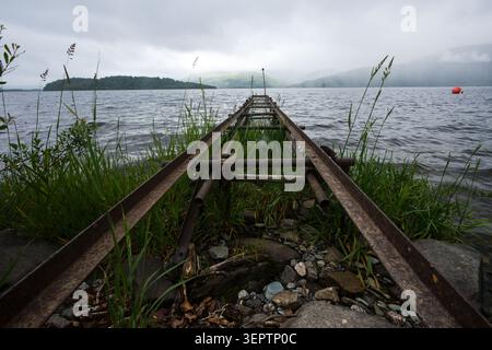 Verlassene Schienen führen an einem nebelbedeckten Tag in den Loch Lomond, West Highland Way, Schottland. Stockfoto