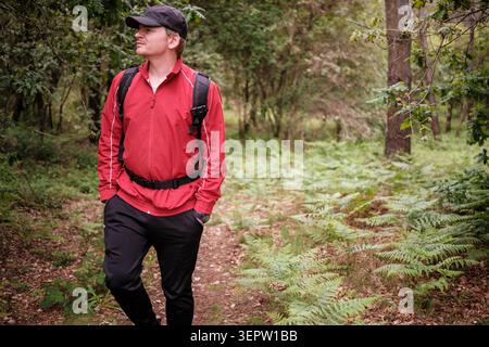 Mann in roter Jacke und Rucksack, der im Wald läuft und wegblickt Stockfoto