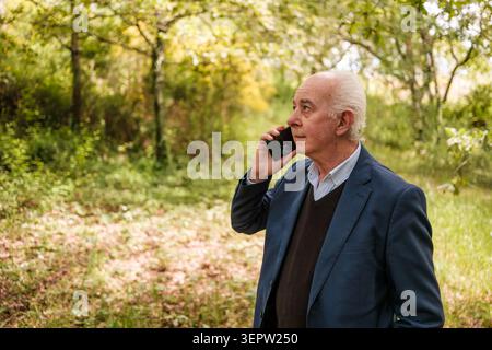 Senior Mann kommuniziert über Smartphone in einer Waldumgebung Stockfoto