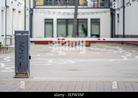 Automatisches Traffic-Boom-Tor, das eine asphaltierte Einfahrt mit Graffiti-Aufschrift auf dem Kontrollposten blockiert, Sicherheitskonzept für Immobilien Stockfoto