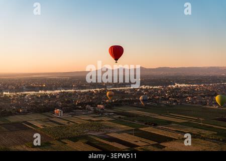 Luftaufnahme der landwirtschaftlichen Landschaft des Niltals nahe Luxor, Ägypten. Ein einzelner Heißluftballon ist in der Ferne über dem grünen Ackerland sichtbar. Blauer Himmel. Stockfoto