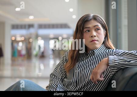 Thai Isan Transgender Geschäftsfrau in den 40ern, die nachdenklich auf dem Sofa drinnen wegschaut. Horizontales Mittelaufnahme-Porträt eines Reifen nicht-binären Südostens Stockfoto