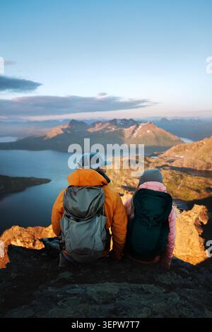 Paare, die gemeinsam wandern, reisen in Norwegen, sitzen zusammen auf Klippen und genießen den Blick auf die Berge bei Sonnenuntergang, Männer und Frauen genießen die Natur, romantischen Urlaub Stockfoto