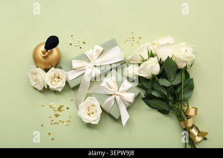 Komposition mit Geschenkboxen, weißen Rosenblüten und einer Flasche Parfüm auf grünem Hintergrund Stockfoto