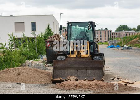 Auf einer Baustelle werden schwere Maschinen eingesetzt. Ein Lader bewegt Sand und Schmutz in der Nähe eines Müllkippers. Im Hintergrund befinden sich neue Gebäude in der Entwicklung. Stockfoto