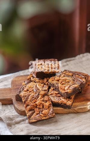 Ein Stapel reichhaltiger Schokoladen-Brownies, die mit Biscoff-Keksbutter verdreht und mit zerquetschten Spekuloos-Keksen auf einem Holzbrett belegt sind. Stockfoto