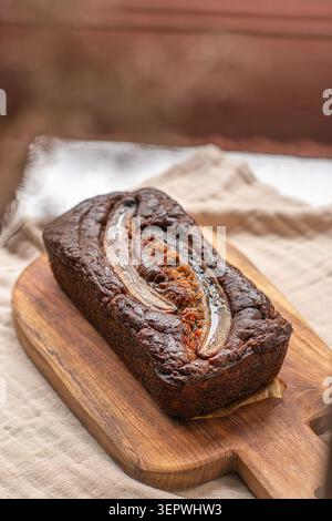 Ein Gourmet-Schokoladen-Bananenbrot mit einer karamellisierten Bananenscheibe, serviert auf einem rustikalen Holzschneidebrett. Stockfoto