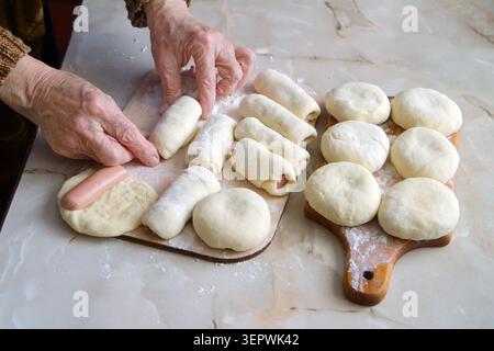 Hausgemachte Kuchen in der Küche kochen. Die Hände einer älteren Frau. Rohe Torten und Würstchen im Teig. Stockfoto