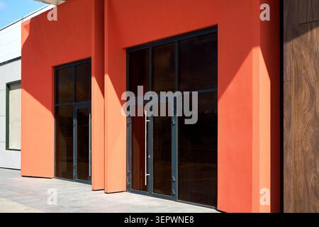 Die moderne Gebäudefassade verfügt über einen hellen orangefarbenen Stuck und elegante Eingangstüren aus Glas mit langen vertikalen Metallgriffen. Saubere architektonische Linien Stockfoto