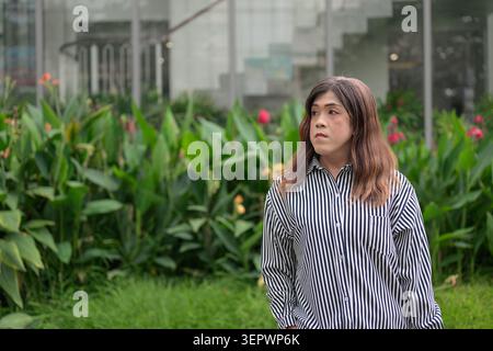 Thai Isan Transgender Geschäftsfrau in den 40ern, die nachdenklich im Freien wegschaut. Horizontales Mittelaufnahme-Porträt eines Reifen nicht-binären Südostasiens Stockfoto