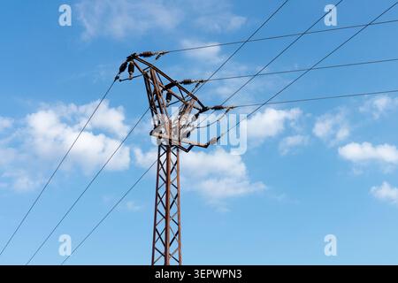 Alte, rostige Stahlgitter-Strommasten mit elektrischen Drähten unter blauem Himmel mit Wolken Stockfoto