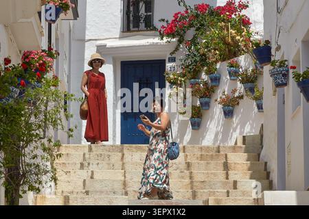 Asiatische Touristen erkunden die San Sebastian Street, eine malerische enge Gasse mit weißen Häusern und Blumentöpfen in Mijas Pueblo, Malaga, Spanien. Stockfoto