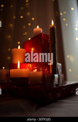 Sanft beleuchtete Kerzen und festliche rote Geschenkboxen schaffen ein gemütliches, warmes Ambiente mit funkelnden Lichtern in einer ruhigen Umgebung, perfekt für einen ruhigen Even Stockfoto