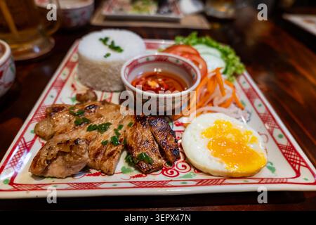 Com tam vietnamesischer Bruchreis mit gegrilltem Schweinekotelett, Spiegelei, eingelegtem Gemüse und Fischsauce, serviert auf traditioneller Keramikplatte Stockfoto