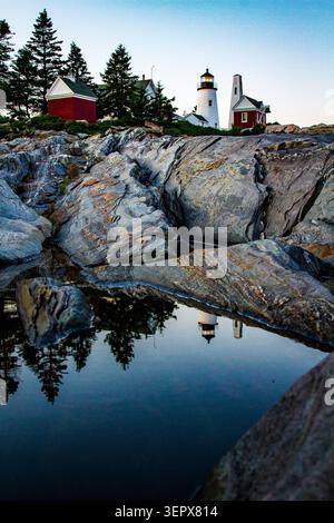 Das Pemaquid Point Lighthouse und sein rotes Glockenhaus spiegeln sich in einem ruhigen Gezeitenbecken auf geschichteten Felsformationen in der Abenddämmerung in Bristol, Maine, wider Stockfoto
