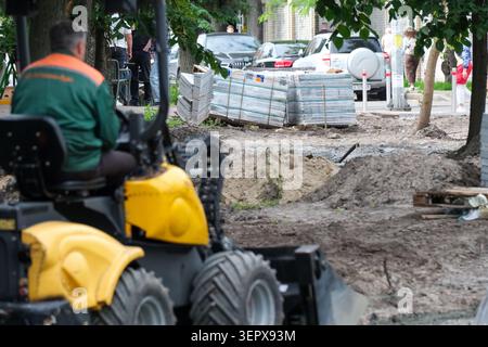 Die Arbeiter sind damit beschäftigt, eine Stadtstraße zu verbessern, während Maschinen frische Materialien einrollen. Kiew, Ukraine, 16. Juni 2026 Stockfoto