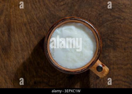 Frische Bio-Sauermilch oder Joghurt oder Sauerrahm in einem rustikalen Tonbecher auf dem Tisch, Nahaufnahme. Draufsicht auf dicken weißen Joghurt, fermentiert oder Sauerrahm Stockfoto