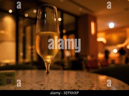 Nahaufnahme eines gekühlten Glases Sekt auf einem Terrazzo-Tisch in einer schwach beleuchteten Luxushotel-Lounge. Stockfoto