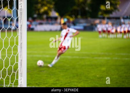 Ein Fußballspieler in weißer Uniform, der während eines Fußballspiels einen Strafschuss in Richtung Tor schießt, gesehen durch das Netz. Stockfoto