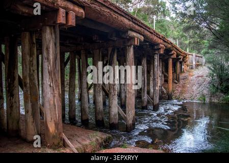 Blick von der Unterseite auf die historische hölzerne Brücke über den fließenden Bach, Gloucester National Park, Western Australia, 10. Juli 2025 Stockfoto