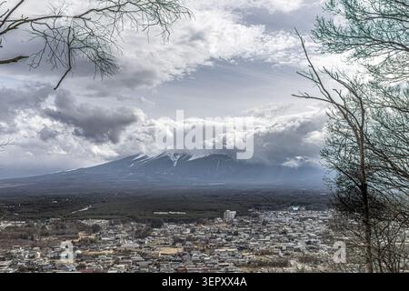 Schneebedeckter Berg Fuji und die Stadt Fujiyoshida, gesehen von einem bewaldeten Aussichtspunkt im Arakurayama Sengen Park, Yamanashi, Japan. Stockfoto
