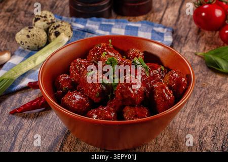 Herzhafte Fleischbällchen in reichhaltiger Tomatensauce, garniert mit frischer Petersilie in einer rustikalen Tonschale auf Holzoberfläche mit Wachteleiern und Tomaten Stockfoto