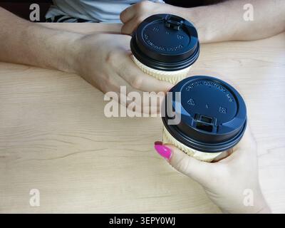Blick von oben auf einen Mann und eine Frau, die Kaffeetassen zum Mitnehmen auf einem Holztisch halten. Stockfoto