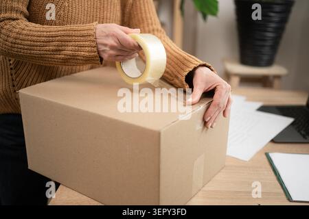 Unternehmerin versiegelt Kartonschachtel mit Verpackungsband, die Boxen für die Lieferung vorbereiten. Nahaufnahme Stockfoto