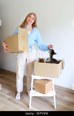 Frau, die sich mit ihrer Katze in eine neue Wohnung einlässt, umgeben von Pappschachteln und frischen Anfängen. Stockfoto