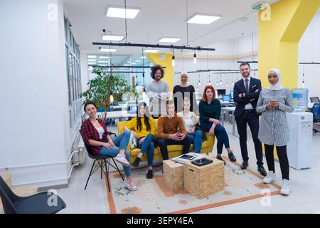 Eine vielfältige Gruppe von neun jungen Berufstätigen, die sich gemeinsam in einem Wohnbereich eines modernen Büros ausgeben. Sie sitzen und stehen, lächeln in die Kamera, Stockfoto