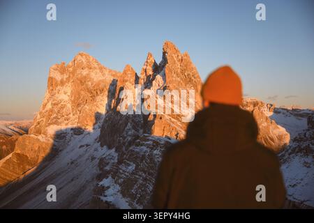 Person, die die schneebedeckten Gipfel von Seceda bei Sonnenuntergang in den Dolomiten bewundert. Dramatische Alpenlandschaft mit zerklüfteten Kalksteinbergen und warmem Abendlicht Stockfoto