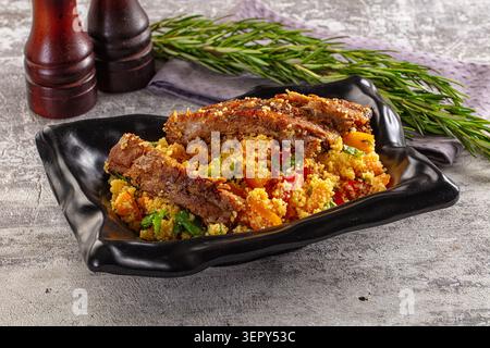 Gebratene Lammrippchen mit Couscous, Gemüse und Rosmarin auf schwarzem Teller Stockfoto