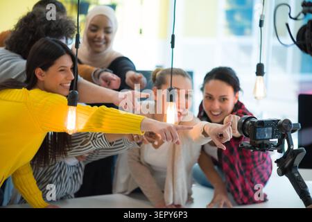Eine lebendige, multiethnische Gruppe junger Unternehmenskollegen versammelt sich eng zusammen, lächelt breit und zeigt mit dem Zeigefinger auf einen Professi Stockfoto