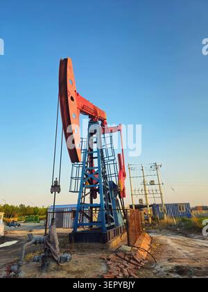 Roter Ölpumpjack bei der Golden Hour in einem chinesischen Produktionshof Stockfoto