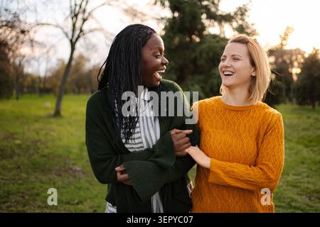 Zwei verschiedene Frauen lachen und spazieren zusammen durch einen Park Stockfoto