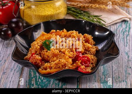 Couscous mit gebratenen Paprika und Tomaten in schwarzer Schüssel auf rustikalem Holztisch. Gesunde Mahlzeit. Vegetarische Speisen. Mediterrane Küche. Nahaufnahme. Körnung Stockfoto