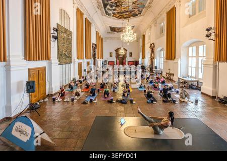 Blick auf den Ballsaal im DomQuartier Salzburg während der Veranstaltung „Pop Up Yoga – Mozart Edition“: An den Wänden hängen historische Wandteppiche (Gobelins), während ein Yogalehrer die Sitzung von einem zentralen Podium aus leitet. Salzburg, Österreich Stockfoto