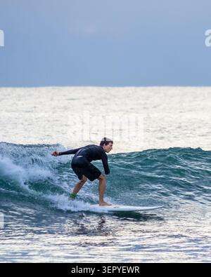 Mirissa, Sri Lanka - 20. Februar 2023: Ein Surfer in einem schwarzen Neoprenanzug reitet auf einem weißen Surfbrett am Mirissa Beach auf einer türkisfarbenen Meereswelle Stockfoto