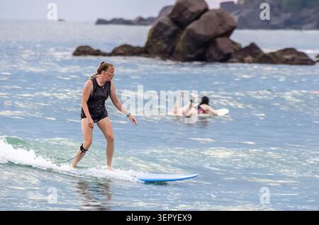 Mirissa, Sri Lanka - 20. Februar 2023: Eine Frau reitet auf einem blauen Longboard auf einer kleinen Welle, während ein anderer Surfer im Hintergrund in der Nähe von ihrem Board fällt Stockfoto