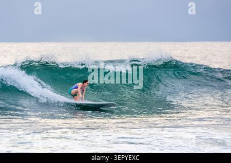 Mirissa, Sri Lanka - 20. Februar 2023: Eine junge Frau in einem bunten Bikini hockt sich auf einem Longboard, während sie auf einer großen, türkisfarbenen Welle in mir reitet Stockfoto