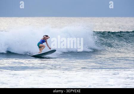 Mirissa, Sri Lanka - 20. Februar 2023: Eine junge Frau in einem bunten Bikini hockt sich auf einem Longboard, während sie auf einer großen, türkisfarbenen Welle in mir reitet Stockfoto